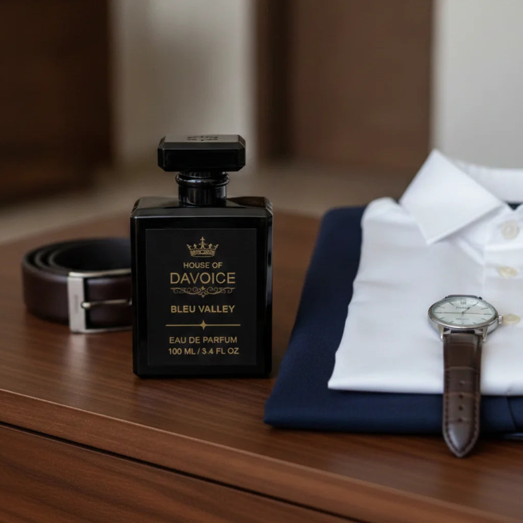 Fresh woody cologne displayed beside a tailored navy blazer, leather belt and classic wristwatch