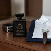 Fresh woody cologne displayed beside a tailored navy blazer, leather belt and classic wristwatch