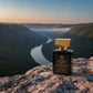 House of DaVoice Mountain Wind fresh woody bergamot cologne that is similar to Savage Dior for men, sitting on a limestone overlook above a scenic river valley at golden hour
